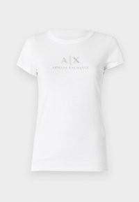 Maglietta bianca in cotone a maniche corte con un logo argentato "A|X ARMANI EXCHANGE" al centro. Collo a giro classico.