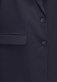 Blazer bleu marine au design élégant, avec une poche avant simple, des revers à cran et deux boutons noirs sur la fermeture avant. Texture de tissu lisse.