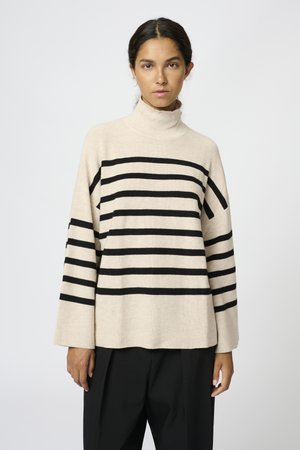 Harmaa turtleneck-neule, jossa on mustia vaakaraitoja, ribbetty pinta, leveät hihat ja rento malli. Yhdistetty mustiin housuihin.