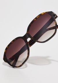  Schildpadbril met een breed, octagonaal frame en gradient bruine glazen. Matte afwerking met subtiele textuur op de armen.