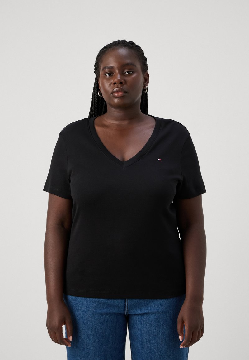 Camiseta negra de manga corta y escote en V, confeccionada con una tela suave, que presenta un pequeño logo en el pecho. Combinada con vaqueros azules.