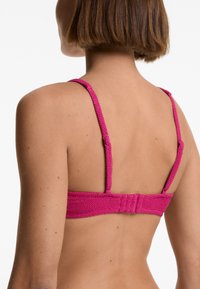 Podprsenka z texturované růžové látky, tenké nastavitelné ramínka a zapínání na háček a očko na zadní straně. Minimalistický design a přiléhavý tvar.
