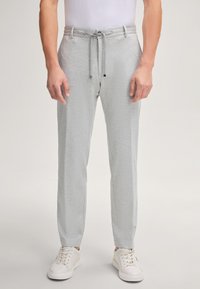 Helle graue Jogginghose mit Kordelzugbund und schmal zulaufenden Beinen. Glatte Stofftextur, kombiniert mit weißen Sneakers.