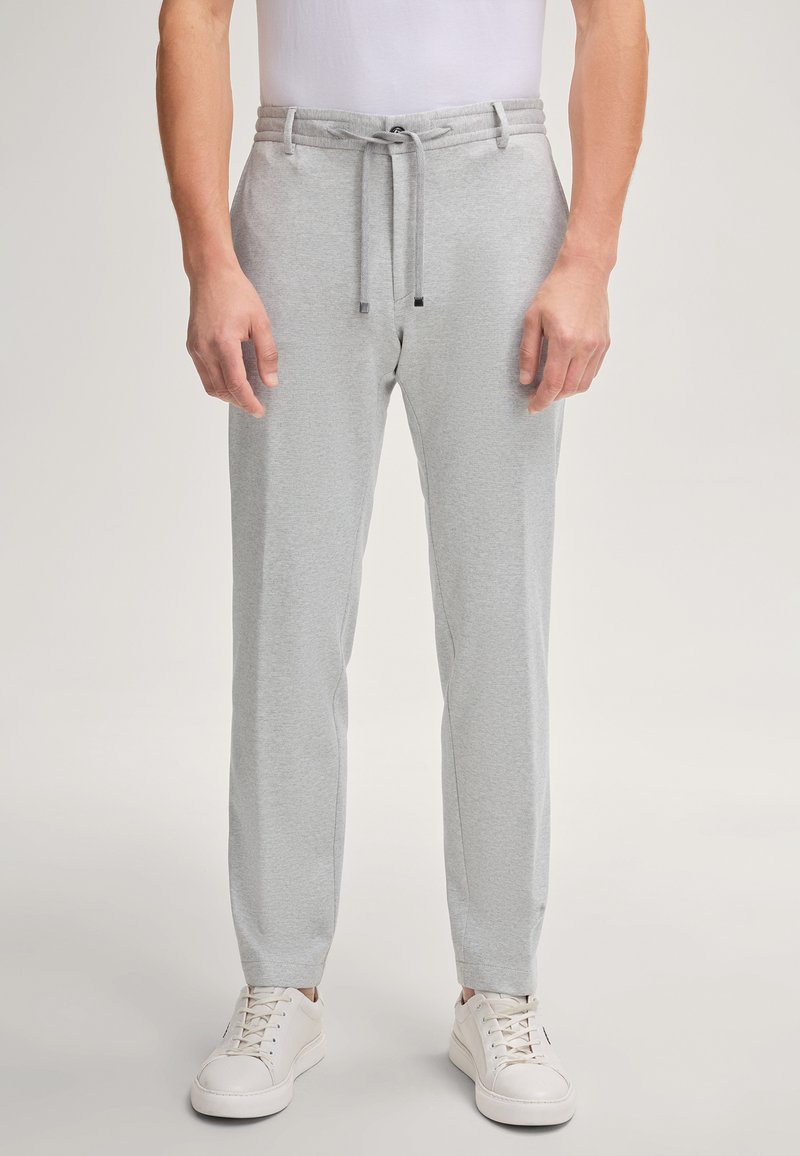 Helle graue Jogginghose mit Kordelzugbund und schmal zulaufenden Beinen. Glatte Stofftextur, kombiniert mit weißen Sneakers.