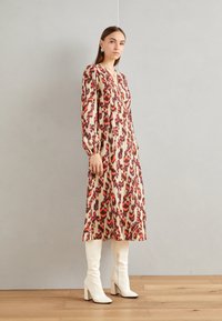 Abito a maniche lunghe con stampa leopardata caratterizzato da tonalità di rosso, rosa e viola su sfondo beige. Abbinato a stivali bianchi al ginocchio.