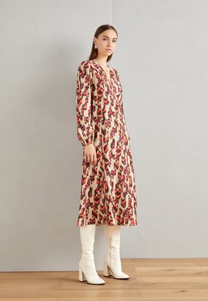 Abito a maniche lunghe con stampa leopardata caratterizzato da tonalità di rosso, rosa e viola su sfondo beige. Abbinato a stivali bianchi al ginocchio.