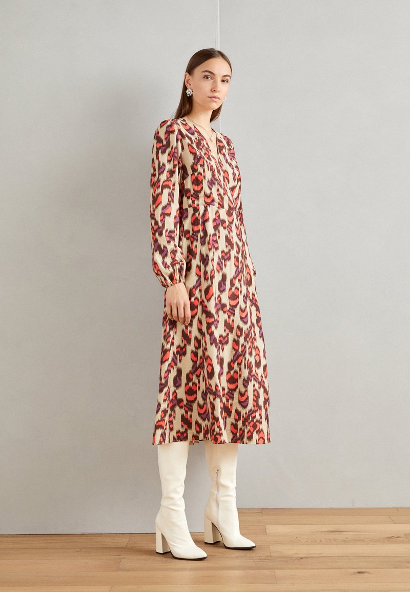Abito a maniche lunghe con stampa leopardata caratterizzato da tonalità di rosso, rosa e viola su sfondo beige. Abbinato a stivali bianchi al ginocchio.