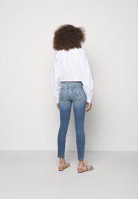 Kapeanit siniset farkut, joissa on haalistunut pesu ja takataskut, joissa on ainutlaatuinen ommeltu kuvio, yhdistettynä valkoiseen pitkähihaiseen puseroon ja sandaaleihin.