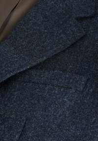 Marineblauer Wollblazer mit strukturierter Oberfläche. Verfügt über einen Reverskragen, eine einzelne Brusttasche und ein feines blaues Punkte-Muster.