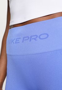 Στενές κολάν υψηλής μέσης Nike Pro από ανοιχτό μπλε ύφασμα με υφή. Περιλαμβάνει ανάγλυφο λογότυπο "NIKE PRO" στη ζώνη της μέσης.
