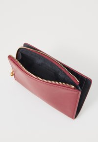 Portefeuille en cuir rouge avec fermeture éclair dorée, doté d'un intérieur doublé de noir et de fentes pour cartes. Texture lisse et forme rectangulaire.