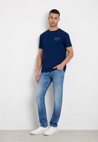 Granatowa koszulka z krótkim rękawem z subtelnym nadrukiem na piersi, w połączeniu z jasnoniebieskimi dżinsami i białymi sneakerami.