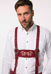 Rød fløjl lederhosen med dekorativ broderi og sølvmetal. Båret over en hvid skjorte med knapper, der har et traditionelt design.