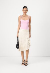 Roze aansluitende bodysuit met dunne bandjes, gecombineerd met een crèmekleurige rok met ruffles en bloemmotieven. Inclusief zwarte ronde tas en sandalen met bandjes.