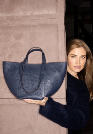 Navy leather handbag with textured surface, rounded shape, and dual handles, positioned against a soft beige background.