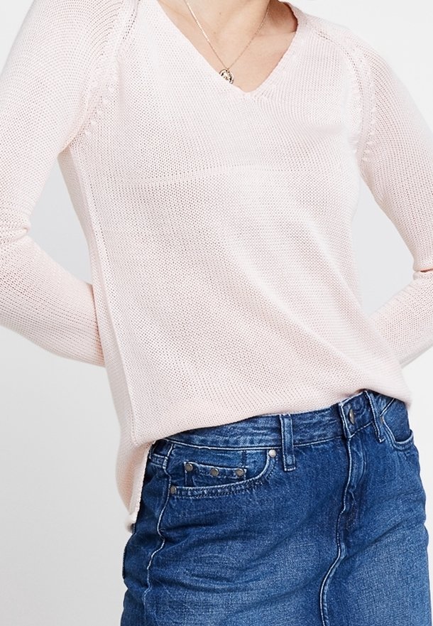 Pull en tricot rose pâle avec un col en V, des manches longues et des accents côtelés ; associé à une jupe en denim avec des détails de boutons.
