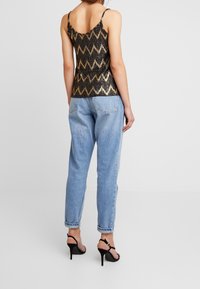 Černý a zlatý tank top se zašímkovanými flitry a vzorem cik-cak, s nastavitelnými ramínky, spárovaný se světlomodrými ohnutými džíny a černými sandály na podpatku.