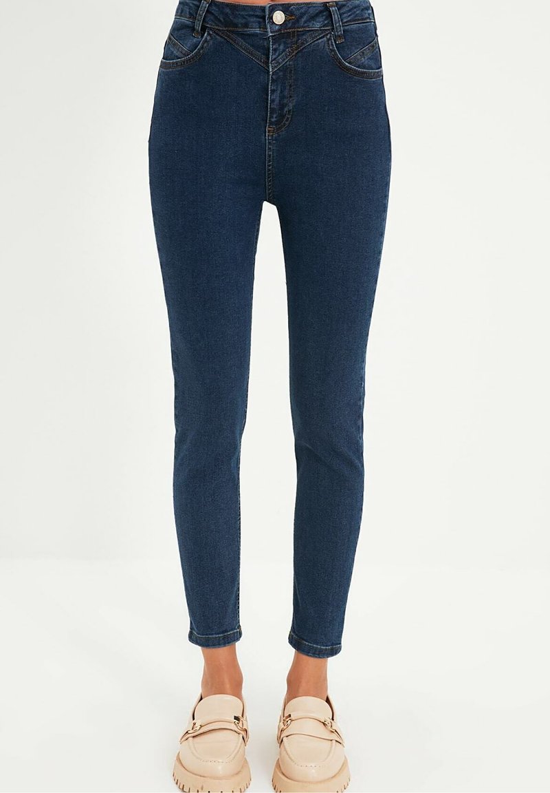 Jean skinny bleu foncé en denim. Design taille haute avec poches classiques et zip, assortis à des chaussures beige à enfiler.