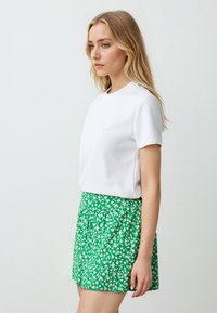 T-shirt bianco a maniche corte abbinato a una gonna verde con piccoli motivi floreali bianchi. La gonna presenta un design plissettato e una vita aderente.