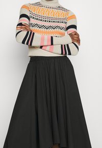 Sweter dzianinowy z wielokolorowymi wzorami geometrycznymi w odcieniach pomarańczowego, różowego, czarnego i beżowego; zestawiony z czarną, zwiewną spódnicą.
