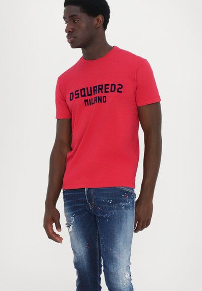 Camiseta de algodón roja con el logo negro "DSQUARED2 MILANO", mangas cortas y un cuello redondo clásico. Se lleva con jeans azules desgastados.