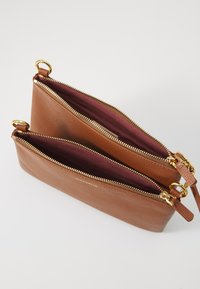 Braune Lederentasche mit strukturierter Oberfläche, ausgestattet mit zwei Reißverschlussfächern, gefüttert mit dunklem Burgunderrot. Goldfarbene Hardware-Akzente.
