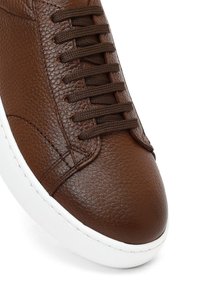 Bruine leren sneaker met een gestructureerd oppervlak, ronde neus, witte rubberen zool en bruine veters.