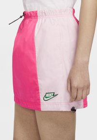 Rosa och ljusrosa Nike-skorts med elastisk midja och dragsko, har grön logotyp och sidodetaljer, med mjukt och glänsande tyg.