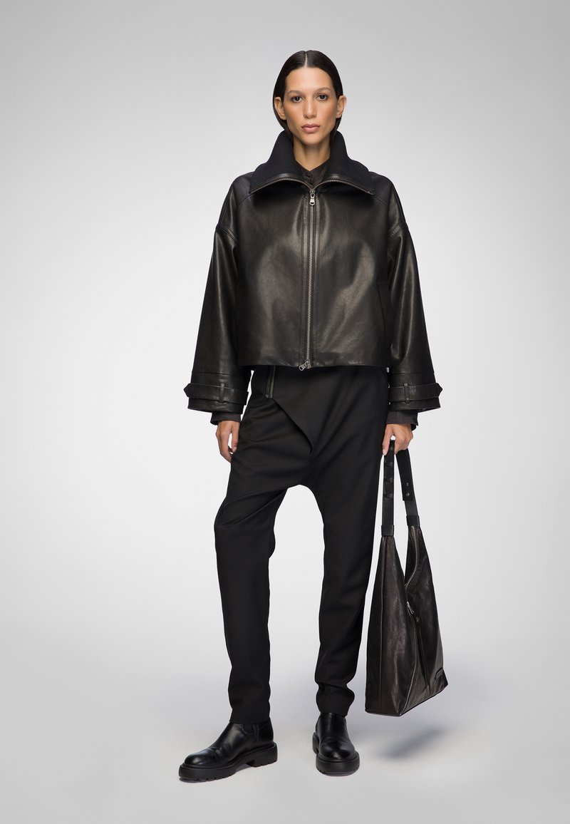 Cropped black leather jacket with a high collar, paired with loose black trousers and black leather boots, holding a dark leather tote bag.