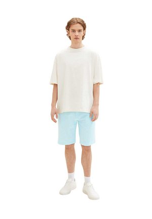 Weißes, übergroßes T-Shirt, hellblaue Shorts und weiße Sneakers. Einfaches Design, kurze Ärmel, lockerer Schnitt und glatte, baumwollähnliche Textur.