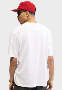 Hvid kortærmet t-shirt med en afslappet pasform, glat bomuldsstof og et enkelt design. Bagfra ses der ingen synlige grafik eller detaljer.
