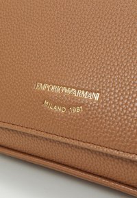 Brązowa torba z teksturowanej skóry z złotym, tłoczonym logo "Emporio Armani" oraz detalem "Milano 1981" z przodu.