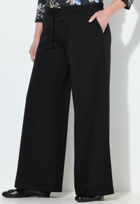 Pantalons larges noirs en tissu doux, dotés d'une taille à cordon de serrage, de poches latérales et d'une texture lisse. Conception simple et polyvalente.