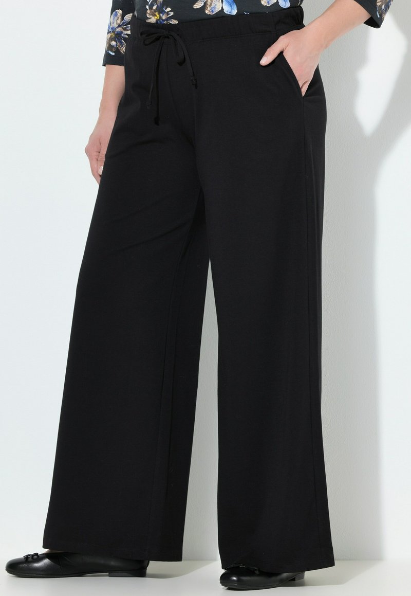 Pantalons larges noirs en tissu doux, dotés d'une taille à cordon de serrage, de poches latérales et d'une texture lisse. Conception simple et polyvalente.