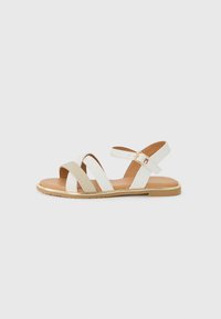 Hvit sandal med beige stoffremmer og såle med gullaccent. Har spenne lukking og åpen tå-design.