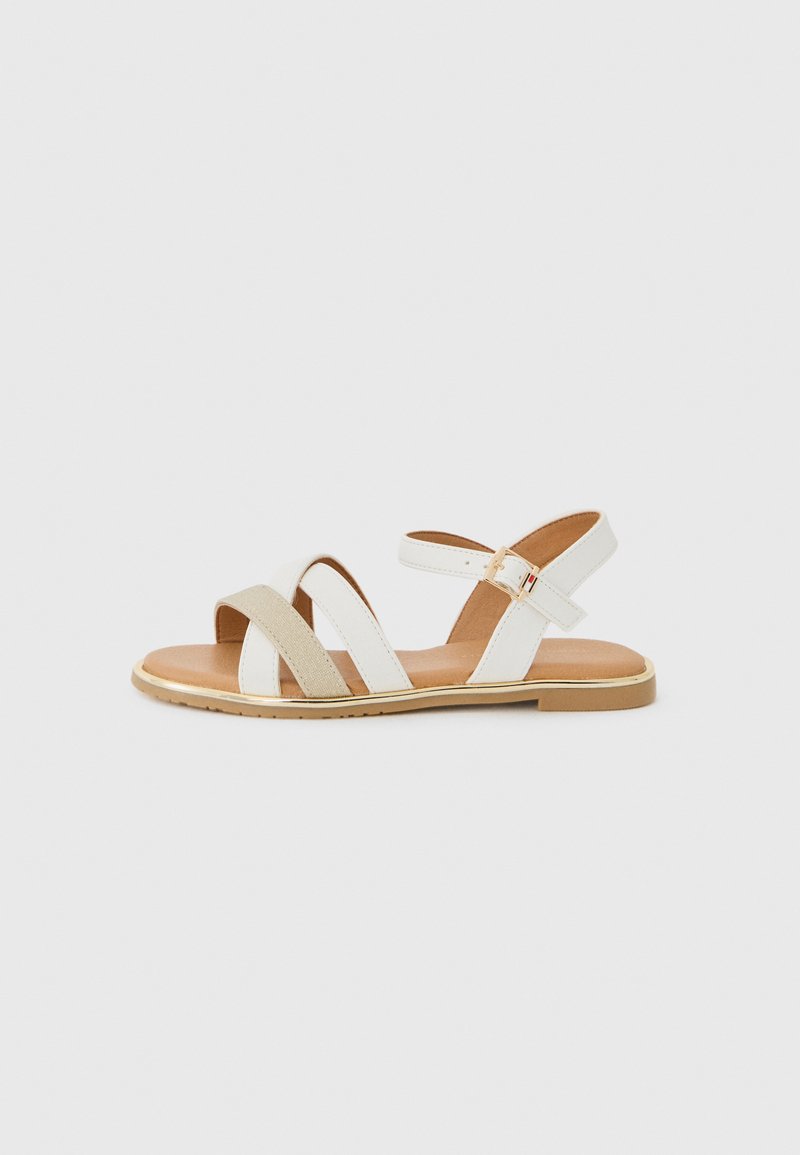 Hvit sandal med beige stoffremmer og såle med gullaccent. Har spenne lukking og åpen tå-design.