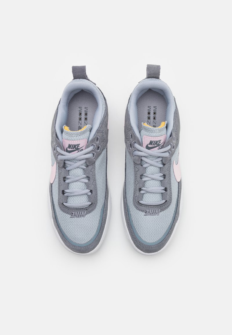 Sneakers Nike avec une tige en mesh gris clair, des accents en daim gris, des détails de logo roses et une languette rembourrée avec une doublure jaune.