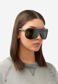 Sivé nadrozmerné slnečné okuliare s gradientnými tmavými šošovkami a geometrickým rámom, s minimálnym kovaním a matným povrchom.