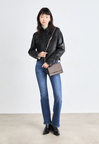 Zwarte cropped leren jas met kraag en voorzakken, gecombineerd met blauwe flared jeans en zwarte enkellaarsjes, met een bruine crossbodytas.