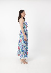 Blomstret maxi kjole med blå, grønne og røde mønstre. Spaghetti stropper, tætsiddende bodice, flydende nederdel. Båret med højhælede sandaler med stropper.