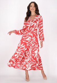 Rochie lungă, roșie, cu modele abstracte albe, având decolteu în V, mâneci lungi și fustă în straturi. Țesătură fină și detalii cu talie strânsă.