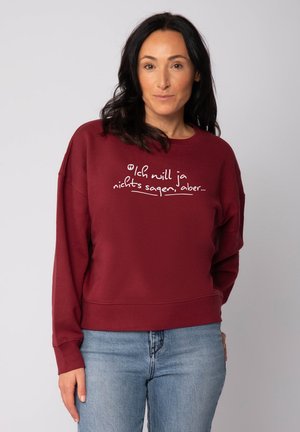 Bordeaux sweatshirt met lange mouwen, ronde halslijn en witte tekst in cursieve letters. Beschikt over een relaxte pasvorm en een zachte textuur.