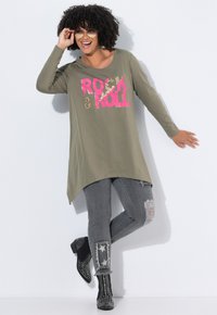 Túnica de manga larga verde oliva con gráfico "ROCK & ROLL" en rosa y estampado de animal. Combinada con jeans grises desgastados y botas de tobillo negras con tachuelas.