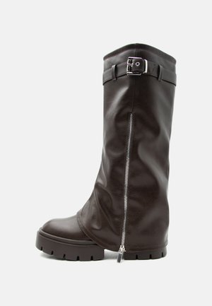 Botte haute en cuir marron foncé avec semelle épaisse, fermeture éclair latérale et bride à la cheville avec boucle argentée, présentée sur fond blanc.