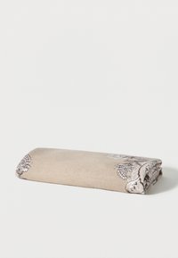 Manta beige doblada con bordado floral blanco y marrón sobre un fondo blanco plano.