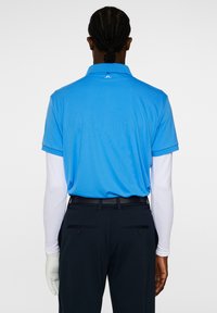 Sininen polo-paita, jossa on kaulus ja lyhyet hihat, yhdistetty mustiin housuihin. Pitkähihainen valkoinen paita alla, kiinnitetty vyöllä.