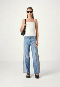 White square-neck top, light blue wide-leg jeans with a distressed finish, black platform sandals, and small black handbag.