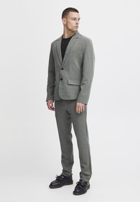 Traje gris de dos piezas hecho de una tela suave, con un blazer de solapa muesca y pantalones ajustados, complementado con zapatos negros.