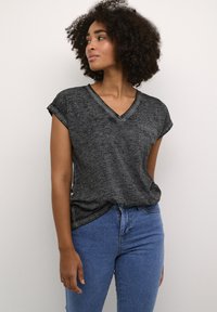T-shirt gris à col en V avec des manches courtes roulées, présentant une poche sur le côté gauche. Associé à un jean bleu clair, sur un fond neutre.
