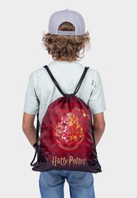 Černo-červený batoh na stažení s motivem znaku Havraspáru a textem "Harry Potter", vyrobený z odolné tkaniny, s černými šňůrkovými popruhy.